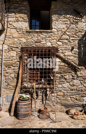 Farm implements, rake, fork,saw, hatchet, axe, and a barrel on a wall with a barred window in the Catalonian village of Beget, Catalonia, Spain Stock Photo