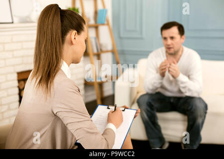 During the session. Nice professional female therapist listening to her patient and taking notes while having a psychological session Stock Photo