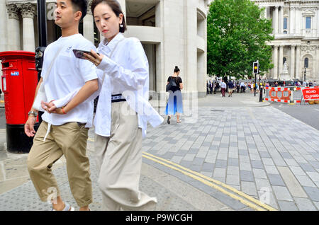 Young Japanese couple near St Paul's Cathedral, London, England, UK. Woman walking and looking her mobile phone Stock Photo