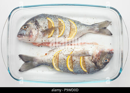 raw dorado raw fish with lemon and vegetables, tomatoes, onions, spices on a glass pan Stock Photo