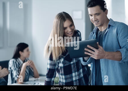 Digital generation. Positive smiling young colleagues using tablet and talking while pleasant businesswoman sitting in the background Stock Photo