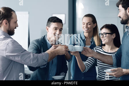 Friendly team. Cheerful smiling young colleagues having a break in the office while drinking coffee and expressing positivity Stock Photo