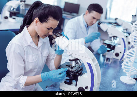Genetic studies. Smart female genetic researcher looking into the microscope and working on her studies while being in the lab