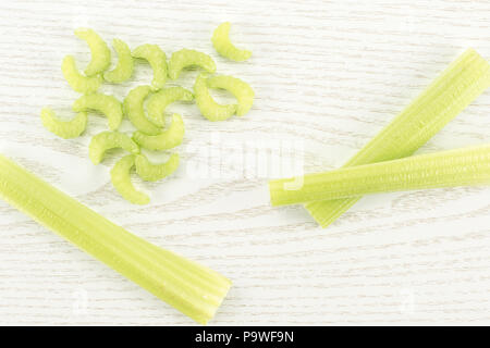 Three green celery sticks with fresh chopped pieces isolated on light wooden background Stock Photo