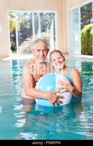 Happy seniors couple with a beach ball in the swimming pool at the spa hotel Stock Photo