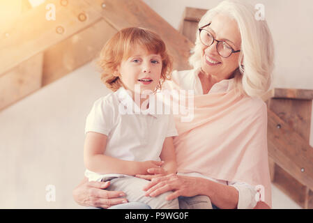 Love him to the moon and back. Beautiful senior woman grinning broadly while looking at her cut little grandson sitting on her lap and looking into th Stock Photo