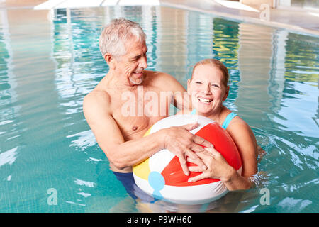 Senior couple has fun with a beach ball in the pool during a spa vacation Stock Photo