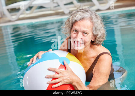 Happy vital senior woman is playing with a ball in swimming pool on vacation Stock Photo
