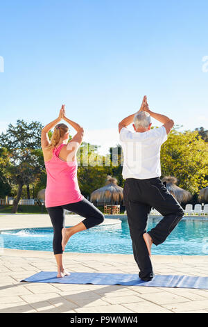 Couple of seniors at the hotel pool doing tree yoga exercise on one leg Stock Photo