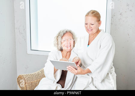 Two senior women in bathrobe at spa hotel using a tablet computer Stock Photo