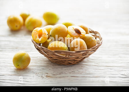 Yellow plums with leaves in a basket on old wooden background close up Stock Photo