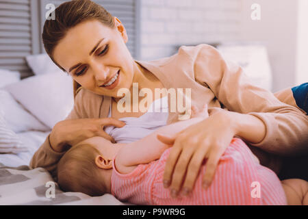 Natural process. Cheerful smiling woman taking care of her little daughter and carefully breastfeeding her Stock Photo