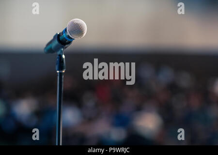 A microphone standing in front of the auditorium on a stand, waiting for a presenter. Big copy space for a message, blurred background. Stock Photo