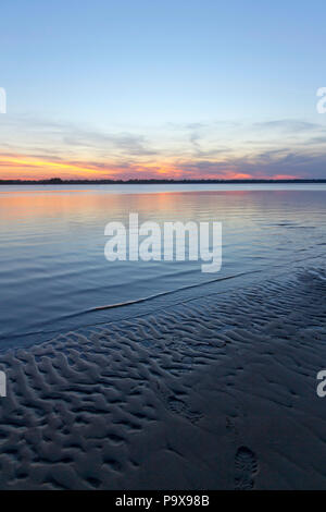 Colorful sunset over an inlet when the water is a low tide exposing water etched textures in the beach sand Stock Photo
