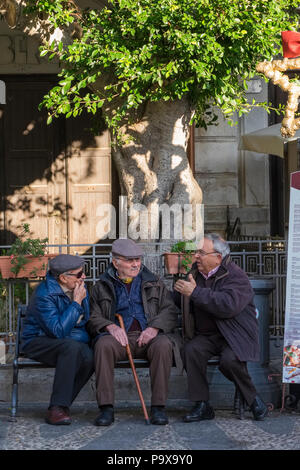Three senior old men - pensioners - in conversation talking on a bench in Italy Stock Photo