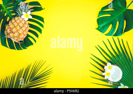 Summer flat lay frame with fresh tropical green leaves, coco and pineapples frame on yellow, retro toned Stock Photo