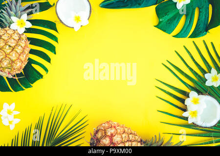 Summer flat lay frame with tropical green leaves, coco and pineapples frame on yellow background, retro toned Stock Photo