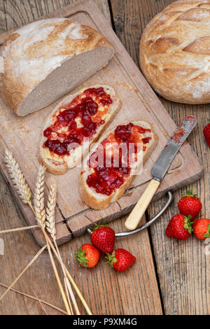 Strawberry jam on bread with wheat and strawberries on a wood background Stock Photo