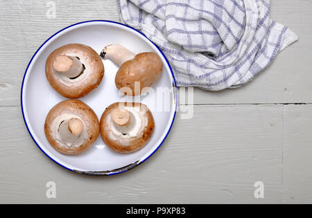 chestnut mushrooms in white metal bowl on painted timber kitchen table top Stock Photo