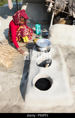 A woman subsistence farmer cooking on a traditional clay oven, using rice stalks as biofuel in the Sundarbans, Ganges, Delta, India. the area is very low lying and vulnerable to sea level rise. All parts of the rice crop are used, and the villagers life is very self sufficient, with a tiny carbon footprint. Stock Photo