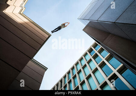 View from below of male parkour athlete jumping from one roof to another Stock Photo