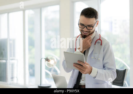 Doctor in hospital working with modern technology for healthy. Friendly man doctor looking and smile for good result of patient data chart. Stock Photo