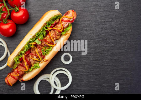 Juicy hot dog and ingredients on dark slate Stock Photo
