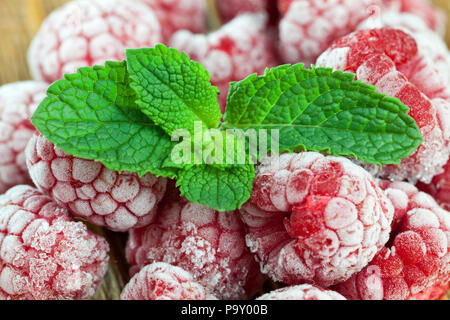 freshly frozen and frosted berries ripe red raspberries in a heap, on berries is a green leaf of fresh mint green, dessert Stock Photo