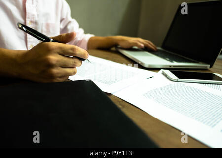 Businessman working at office with laptop and documents on the table, Businessman holding pens and papers taking notes in documents on the table. Stock Photo