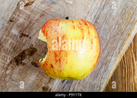 lying on a wooden cutting board on the side of the side red and yellow apple that once bitten, closeup Stock Photo