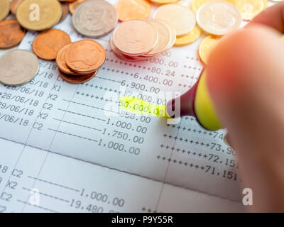 Close-up hand with yellow marker pen highlighting on the deposit money, account statement in saving account passbook with gold, silver and copper coin Stock Photo