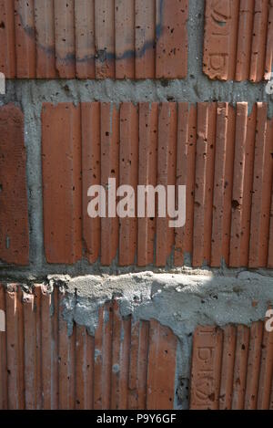 Stylish corrugated red clay bricks, brickwork with gray cement as construction work of builders. Stock Photo