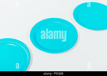 Three blue disposable plates of on white table, flat lay. Minimal top view composition with hard light. Stock Photo