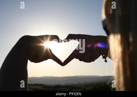 Woman making a heart shape with her hands showing the sun light shining through. Stock Photo