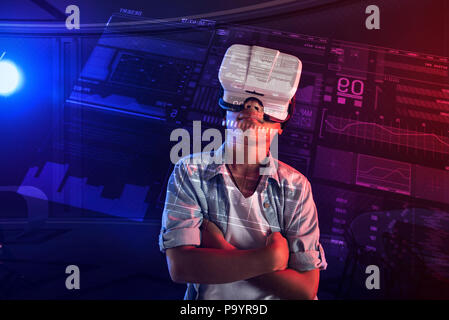Dreamy boy standing with his arms crossed and using virtual reality glasses Stock Photo