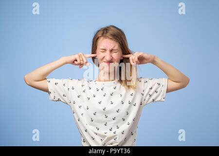 Portrait of funny european woman plugging ears, closing her eyes, pretending not to hear wat she is told standing on blue background Stock Photo