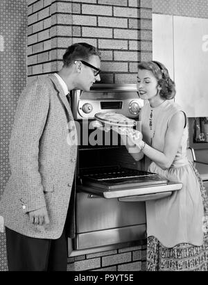 1950s COUPLE IN KITCHEN WOMAN SHOWING FRESHLY BAKED PIE TO MAN - bx016757 CAM001 HARS 1 HOUSEHOLD STYLE WELCOME SMELL DESIGN PLEASED JOY SATISFACTION FEMALES VERTICAL MARRIED SMELLING SHOWING SPOUSE HUSBANDS HEALTHINESS COPY SPACE HALF-LENGTH LADIES PERSONS CARING MALES B&W NERD FRESH HAPPINESS CHEERFUL BAKE CAM001 PRIDE HOUSEWIVES SMILES JOYFUL PIES STYLISH MID-ADULT MID-ADULT MAN MID-ADULT WOMAN TOGETHERNESS WIVES AROMA BLACK AND WHITE CAUCASIAN ETHNICITY HOUSE WIFE OLD FASHIONED WALL OVEN Stock Photo