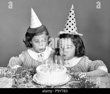 1960s TWIN GIRLS WEARING PARTY HATS BLOWING OUT CANDLES ON BIRTHDAY CAKE - j12268 HAR001 HARS HALF-LENGTH INSPIRATION MATCH CARING SIBLINGS SPIRITUALITY SISTERS B&W MATCHING SAME HAPPINESS HEAD AND SHOULDERS EXCITEMENT RECREATION SIBLING STYLISH LOOK-ALIKE DUPLICATE GROWTH JUVENILES LOOK ALIKE TOGETHERNESS BLACK AND WHITE CAUCASIAN ETHNICITY CLONE HAR001 OLD FASHIONED Stock Photo