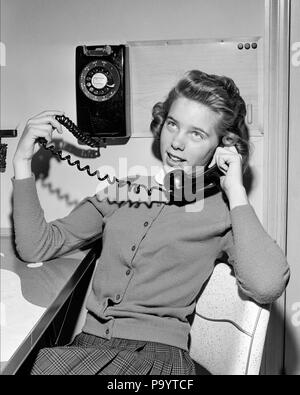 1950s TEENAGE GIRL TALKING ON WALL MOUNTED DIAL TELEPHONE HOLDING THE COILED PHONE CORD TO THE HANDSET - j9197 HAR001 HARS FRIENDSHIP HALF-LENGTH ADOLESCENT PERSONS TEENAGE GIRL ENTERTAINMENT GOSSIPING EXPRESSIONS B&W CORD FREEDOM DIAL HAPPINESS EXCITEMENT RECREATION HOPEFUL PHONES CONNECTION TELEPHONES COILED TEENAGED HANDSET JUVENILES MOUNTED BLACK AND WHITE CAUCASIAN ETHNICITY HAR001 OLD FASHIONED WALL PHONE Stock Photo
