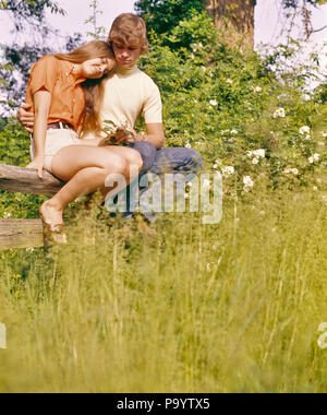 1970s ROMANTIC TEENAGE COUPLE SITTING ON WOODEN FENCE IN FIELD - kj6253 HAR001 HARS HEALTHINESS COPY SPACE FRIENDSHIP HALF-LENGTH ADOLESCENT PERSONS BOYFRIEND CARING MALES TEENAGE GIRL TEENAGE BOY DATING GIRLFRIEND HAPPINESS LOW ANGLE LOVING CONNECTION CUDDLING AFFECTIONATE CUDDLE FRIENDLY STYLISH TEENAGED YOUNG LOVE PUPPY LOVE AFFECTION JUVENILES TOGETHERNESS CAUCASIAN ETHNICITY HAR001 OLD FASHIONED Stock Photo