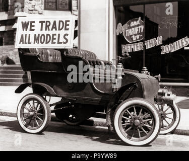 1930s ANTIQUE CAR WITH WE TRADE ALL MODELS ADVERTISING SIGN PARKED ON STREET IN FRONT OF CAR DEALERSHIP - m1583 HAR001 HARS BLACK AND WHITE HAR001 OLD FASHIONED Stock Photo