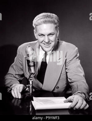 1950s SMILING MIDDLE AGED MAN NEWSMAN ANNOUNCER  TALKING INTO MICROPHONE LOOKING AT CAMERA - r4379 HAR001 HARS FACIAL STYLE COMMUNICATION BLOND COMPETITION PLEASED JOY LIFESTYLE JOBS HALF-LENGTH PERSONS MALES ENTERTAINMENT CONFIDENCE EXPRESSIONS B&W EYE CONTACT FREEDOM PERFORMING ARTS SKILL SUIT AND TIE OCCUPATION SKILLS CHEERFUL ANNOUNCER HONEST EXCITEMENT KNOWLEDGE AUTHORITY OCCUPATIONS POLITICS SMILES CONNECTION JOYFUL REPORTING STYLISH TRUSTWORTHY WIDE LAPELS SINCERE MID-ADULT MID-ADULT MAN NEWSMAN ANNOUNCING BLACK AND WHITE CAUCASIAN ETHNICITY COMMENTATOR HAR001 OLD FASHIONED Stock Photo