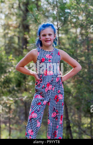 Atrtractive 8 year old girl, in colorful jump suit, hair is dyed bright blue, looking at camera and standing in the trees. Model Release #113 Stock Photo