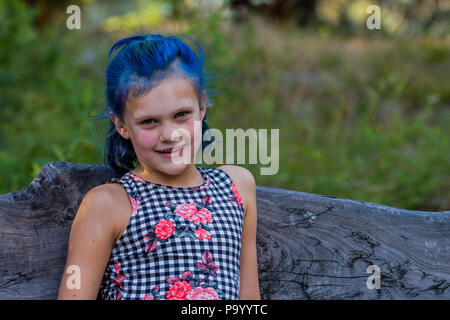 Atrtractive 8 year old girl, in colorful jump suit, hair is dyed bright blue, looking at camera and sitting on bench. Model Release #113 Stock Photo