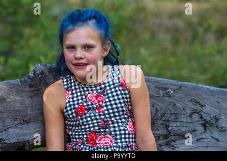 Atrtractive 8 year old girl, in colorful jump suit, hair is dyed bright blue, looking at camera and sitting on bench. Model Release #113 Stock Photo