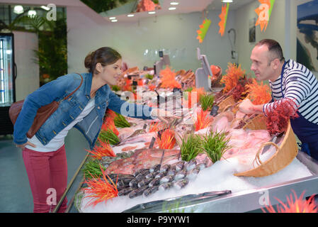 smiling female customer choosing and buying fish in shop Stock Photo