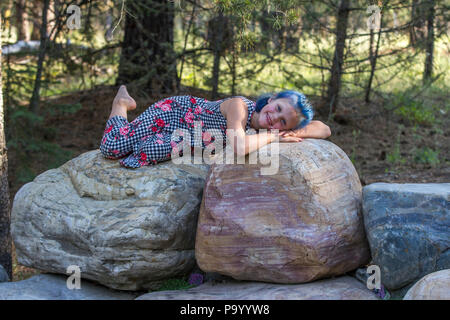 Atrtractive 8 year old girl, in colorful jump suit, hair is dyed bright blue, looking at camera laying on rock, smiling at cameraModel Release #113 Stock Photo