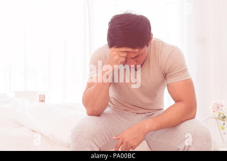 Depressing asian man is siiting on bed with headache Stock Photo