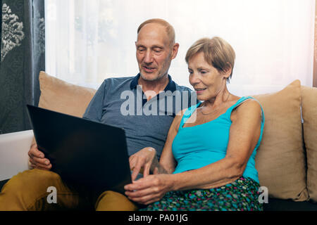 senior couple sitting in sofa and using laptop together at home Stock Photo