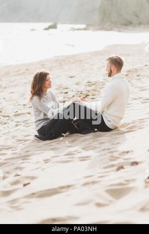 Happy man and woman sitting on sand near sea, romantic mood Stock Photo